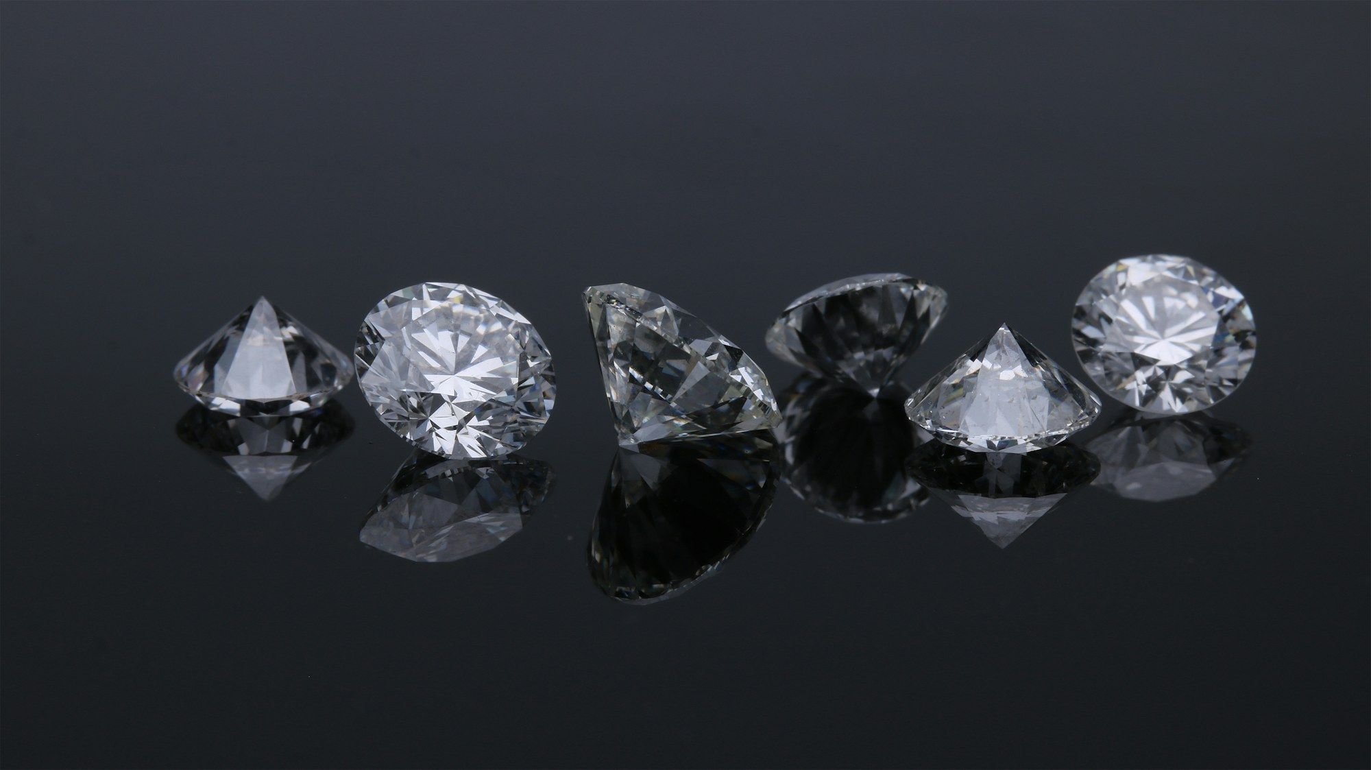 Row of loose diamonds in different shapes on dark grey